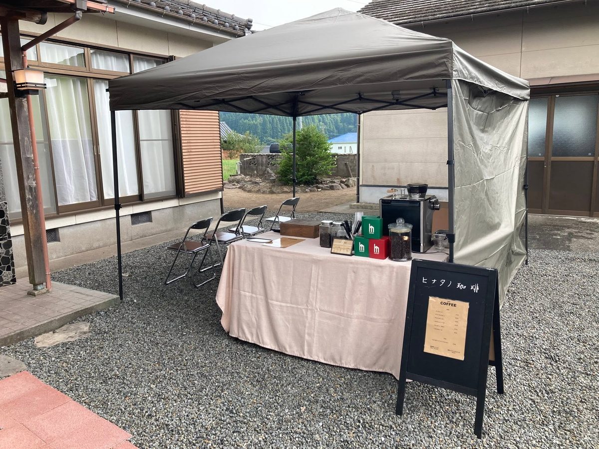 家屋の前にタープを張った珈琲の出店。メニュー看板と焙煎豆、グラインダー、椅子が並ぶ