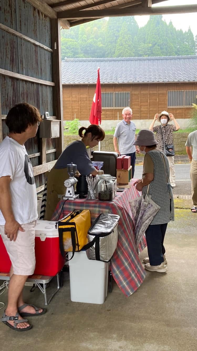 納屋の土間でコーヒーを淹れ、地域の人が受け取りに来ている。背景に杉山と瓦屋根の蔵